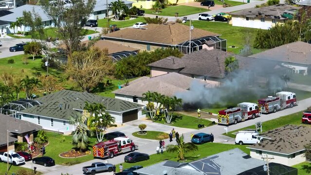 Aerial view of house on fire and firefighters extinguishing flames after short circuit caused spark to ignite wooden roof damaged by hurricane Ian wind. Home disaster in Florida suburban area