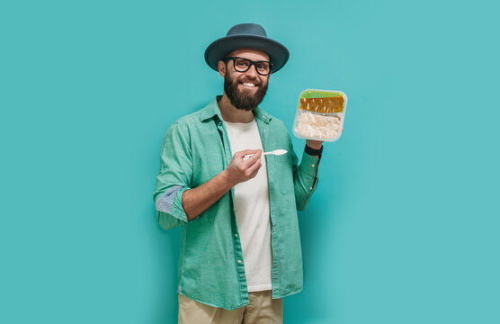 A young guy with a beard holds in his hand ready food from the supermarket in plastic packaging for lunch. Fast food concept