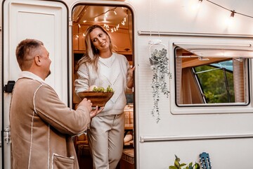 Family trailer travel. Dad, mom in cozy knitted sweater. Picnic in nature.Holiday barbecue BBQ food.Romantic vacation weekend dinner.Road lunch snack.Camper,house on wheels