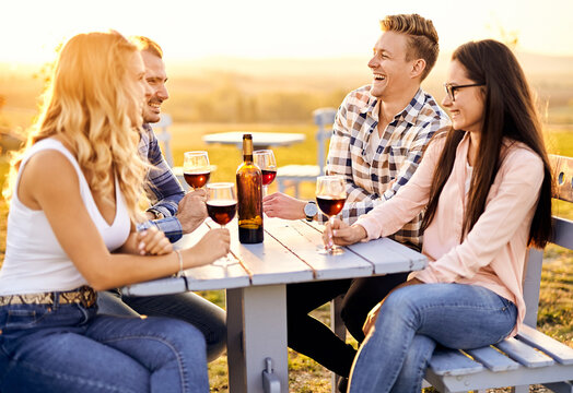 Young friends having fun outdoors - Happy people enjoying harvest time together at farmhouse winery countryside - Youth and friendship concept - Tasting red wine at vineyard before sunset