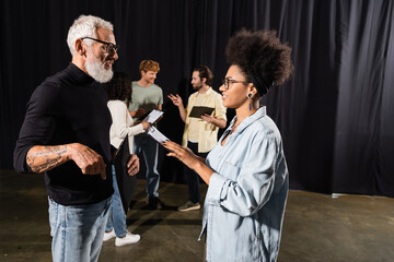 african american actress with clipboard looking at screenwriter near actors in acting school....