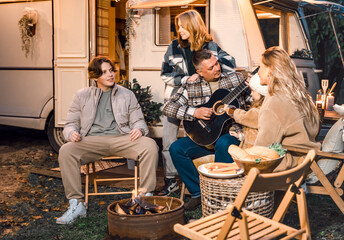 Family trailer travel.Children,brother sister,mom dad playing guitar,singing song at fire.Evening picnic in nature.Holiday barbecue BBQ food.Vacation weekend dinner.Road lunch.Camper,house on wheels