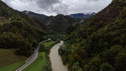 Fototapeta na wymiar Rainy day in Slovenia. Wet asphalt road along the mountain river. Close clouds in mountains. Weekend road trip. Drone photo.