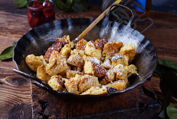 Traditioneller österreichisch Kaiserschmarren mit Zwetschgen und Rosinen serviert als close-up in einer rustikalen schmiedeeisernen Bratpfanne 