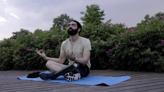 Fit man with disability wearing bionic hi-tech leg prosthesis doing meditation routine outdoor