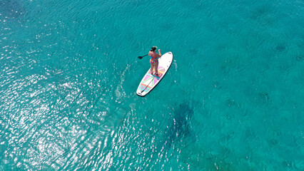 Aerial drone photo of unidentified young woman enjoying stand up paddle board or SUP in tropical...