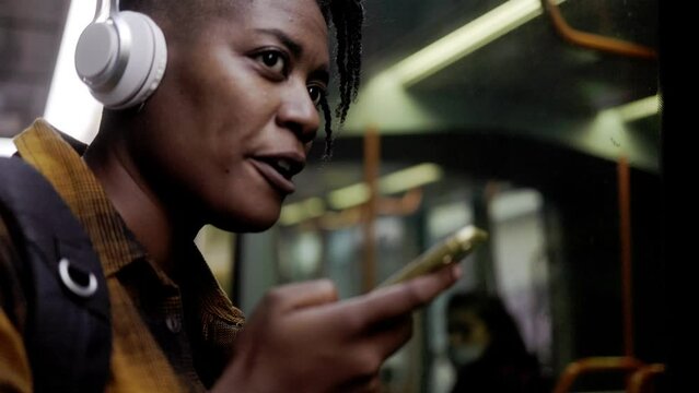 African young woman talking on mobile phone while waiting at bus station outdoor
