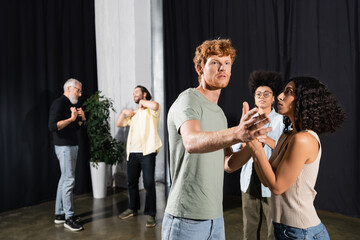 redhead man pointing with hand near interracial actresses and actors on blurred background.