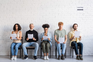 interracial actors reading scenarios while sitting on chairs and waiting for casting.