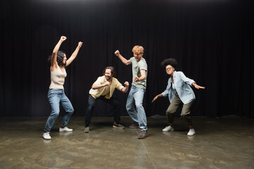 full length of excited interracial students posing in acting skills studio.