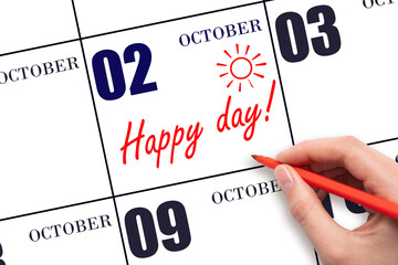 Hand writing the text HAPPY DAY and drawing the sun on the calendar date October 2