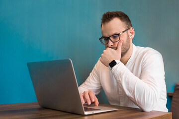 Attractive guy young European businessman works in a laptop sitting at a table in a cafe