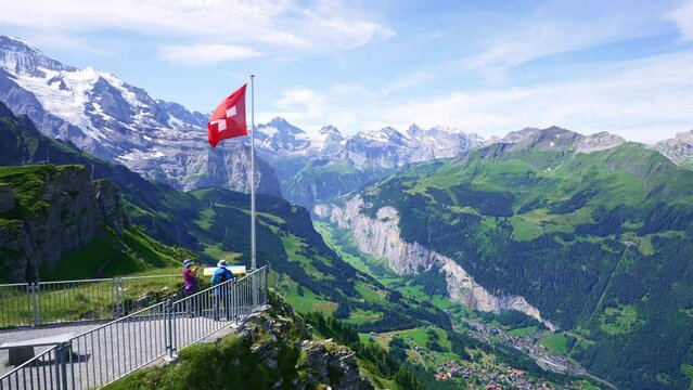 Swiss flag waving, tourists admire peak of Jungfrau mountain on Mannlichen viewpoint, Bernese Oberland in Switzerland