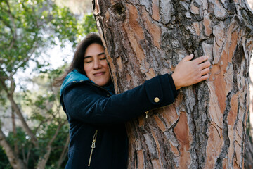 Latina girl hugging a tree in nature while smiling and meditating in contact with nature