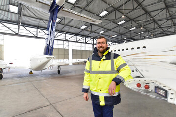 Portrait of an aircraft mechanic in a hangar with jets at the airport - Checking the aircraft for safety and technical function - 566782650