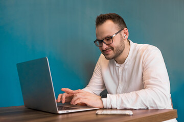 A young European businessman with glasses and a white shirt works in a laptop sitting at a table in a cafe