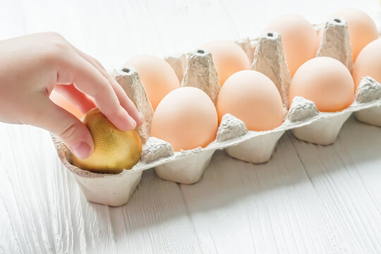 The child takes out a golden egg from the egg tray. A dozen chicken eggs on the table. Rise in price of products in Ukraine. New egg prices