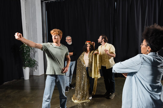 Multiracial Woman In Queen Costume And Redhead Man With Outstretched Fist Rehearsing Scene In Acting Skills School.