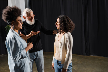 smiling art director pointing with hand and talking to multiracial woman near african american...