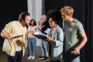 Fototapeta na wymiar young multicultural actors looking at screenplay during rehearsal in acting skills studio.