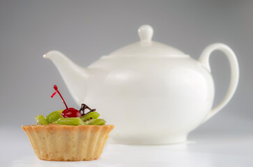 Colorful fruit cake made with kiwi, candied cherry and chocolate on a grey background with a teapot.