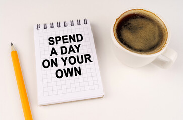 On a white surface, a cup of coffee, a pencil and a notepad with the inscription - Spend a day on your own