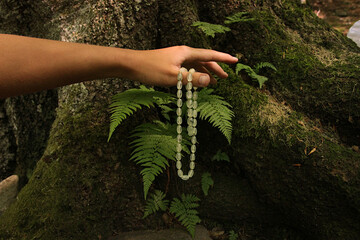 Green faceted beads made of grossular (pomegranate) in the hand opposite the fern bush.