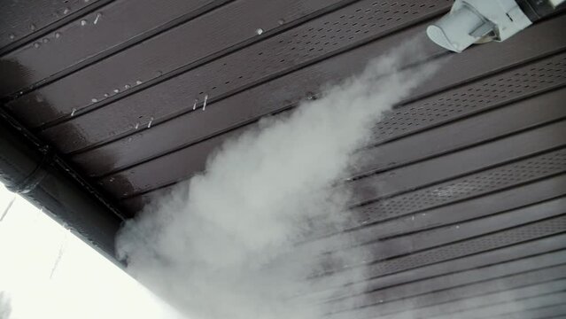 Slow motion video of steam from a chimney under the roof of a house in winter. Pipe from the sauna against the background of the sky and the roof of the building.