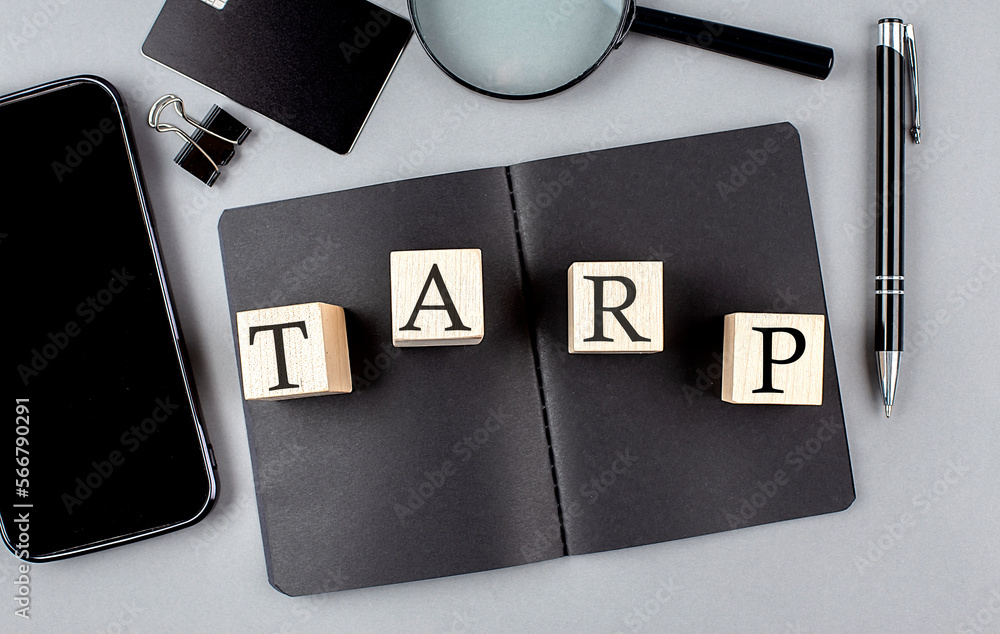 Poster word tarp troubled asset relief program on wooden block on black notebook with smartpone, credit car