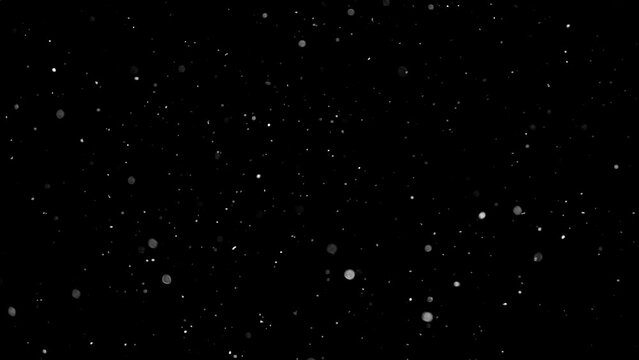 The snow slowly flies at night. White dust and glitter on a black background.