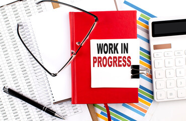 WORK IN PROGRESS text on sticky on red notebook on the chart background