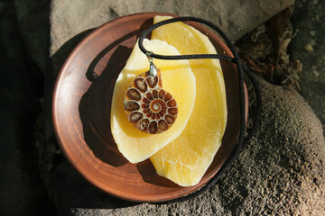 A pendant made of precious ammonite on the background of a clay plate with dried mango.