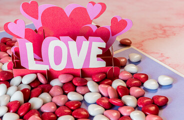 Valentine's day greeting card with red chocolate hearts around it on a pink marble table. The party of the lovers