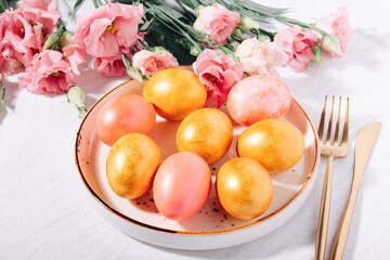 Gold and pink painted Easter eggs in pastel colors in a plate on a white cotton tablecloth