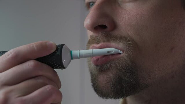 Close-up of man cleaning teeth by an ultrasonic toothbrush. Male brushing his teeth with electric teethbrush. Theme oral health and dental hygiene. Morning sanitation procedures in the bathroom. 