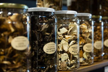 Various dried mushrooms in closed glass jars for sale on counter in store - obrazy, fototapety, plakaty