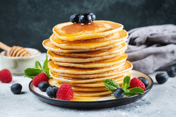 Delicious pancakes, with fresh blueberries, raspberry and maple syrup or honey on a dark background