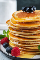 Delicious pancakes, with fresh blueberries, raspberry and maple syrup or honey on a dark background