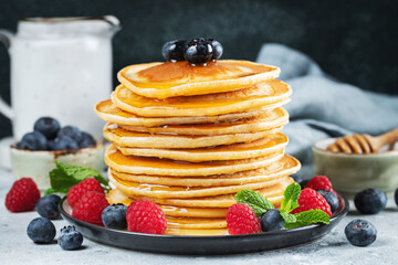 Delicious pancakes, with fresh blueberries, raspberry and maple syrup or honey on a dark background