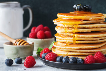 Delicious pancakes, with fresh blueberries, raspberry and maple syrup or honey on a dark background