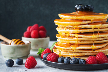 Delicious pancakes, with fresh blueberries, raspberry and maple syrup or honey on a dark background