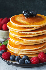 Delicious pancakes, with fresh blueberries, raspberry and maple syrup or honey on a dark background