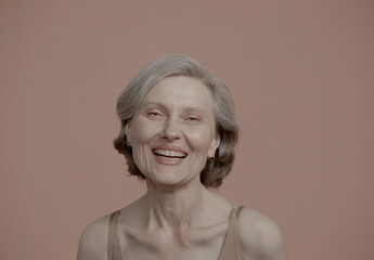 Portrait of 60s adult mature Caucasian female smiling and laughing at camera against pastel colored...