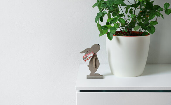 Easter bunny statuette near a plant ina white flower pot on a shelf, easter minimal concept, copy space