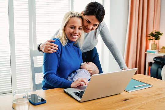 Gay lesbian couple of mothers and newborn baby working with laptop computer at home - Lgbt family concept - Focus on infant face