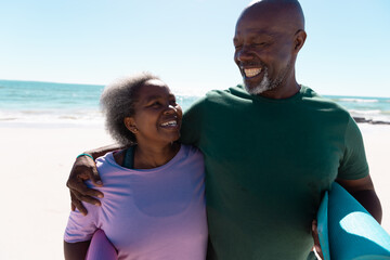 African american senior couple with yoga mats looking at each other against sea and clear sky