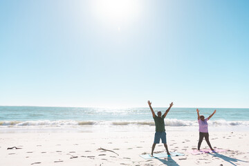 African american senior couple with arms raised exercising at beach against sea and clear blue sky