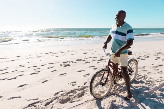 Image of african american man on bike on beach by sea