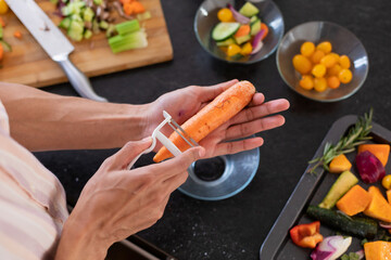 Midsection of biracial man cooking, peeling carrot in kitchen