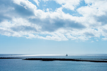 Obraz premium Seascape and cloudscape in blue color. Calm sea on a sunny day with clouds horizontal landscape background. Distant boat silhouette in the ocean.